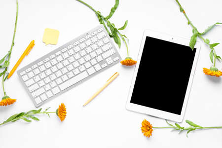 Tablet with computer keyboard, pens, sticky note and flowers on white backgroundの写真素材