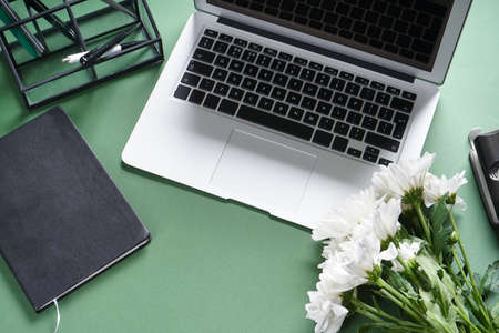 Laptop with stationery and flowers on green backgroundの写真素材
