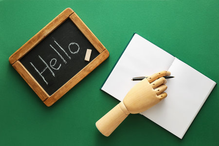 Chalk board with word HELLO, wooden hand, pen and notebook on green backgroundの写真素材