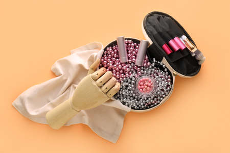 Makeup bag with beads, decorative cosmetics, brushes and wooden hand on beige background