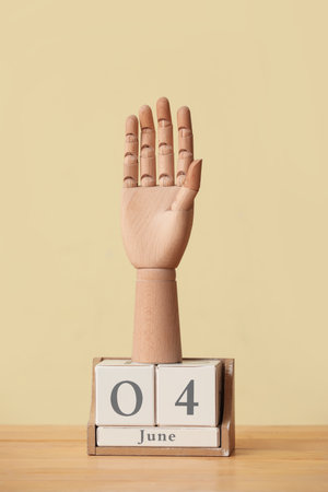 Wooden hand with cube calendar on table against yellow background