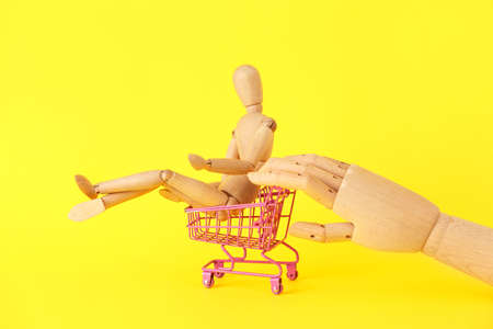 Wooden hand with mannequin and shopping cart on yellow backgroundの写真素材