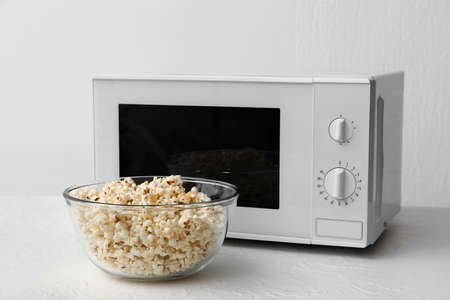 Bowl with popcorn near microwave oven on light backgroundの写真素材
