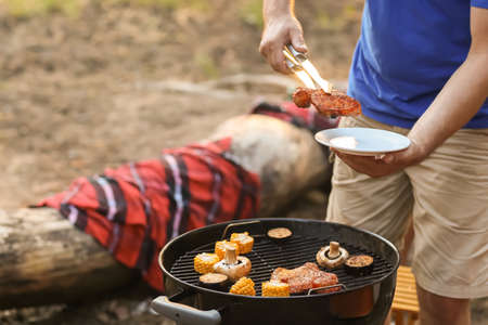 Young man putting grilled meat on plate at barbecue party, closeup