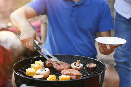 Handsome man putting grilled meat on plate at barbecue party, closeupの写真素材