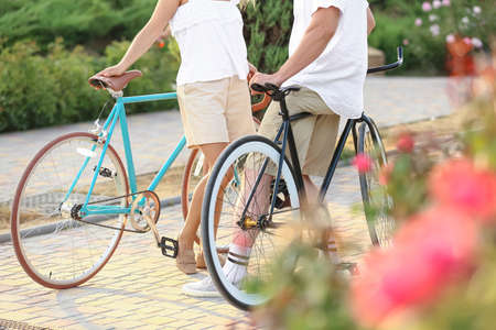 Mature couple with bicycles walking in city park on summer dayの写真素材