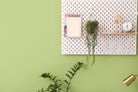Pegboard with stylish decor, houseplants and notebook on color wallの写真素材