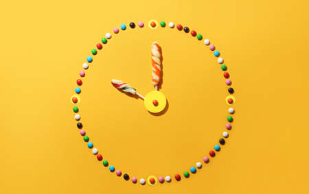 Clock made of colorful candies and lollipops on color backgroundの写真素材
