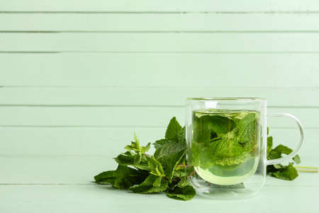 Glass cup of tasty mint tea on green wooden background