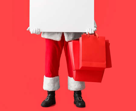 Santa Claus with blank poster and shopping bags on color background