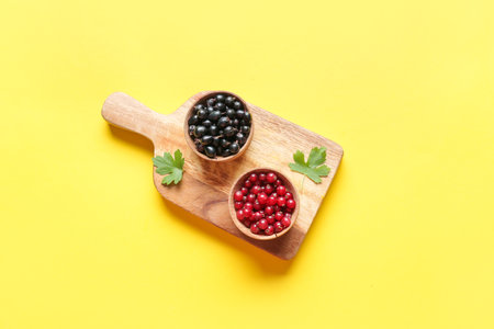Bowls with ripe red and black currant on color background