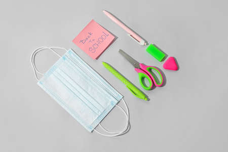 Paper with text BACK TO SCHOOL, stationery and medical mask on light background