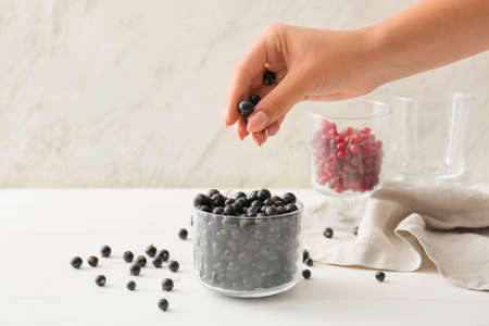 Female hand with tasty black currants on light wooden background