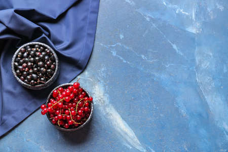 Bowls with ripe red and black currant on color background
