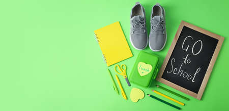 Board with text GO TO SCHOOL, stationery, lunch box and shoes on color backgroundの写真素材
