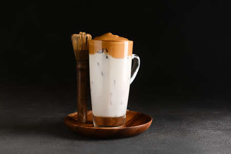 Glass cup of tasty dalgona hojicha latte and chasen on dark backgroundの写真素材