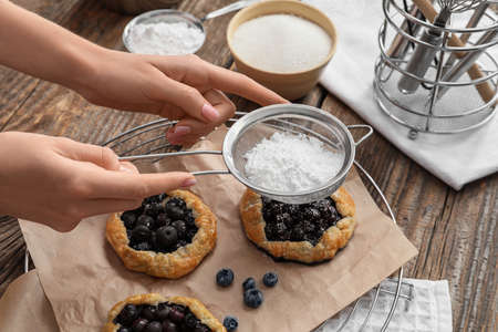 Woman sprinkling tasty blueberry galettes with sugar powder on wooden backgroundの写真素材