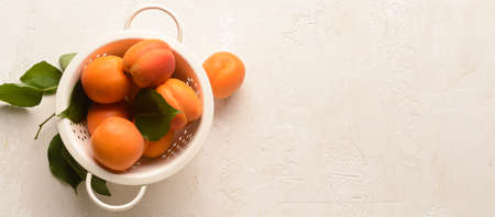 Colander of tasty ripe apricots on light background with space for text