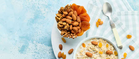 Bowls with tasty sweet oatmeal, dry apricots and nuts on blue background with space for text