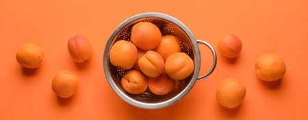 Colander with tasty ripe apricots on orange background, top view