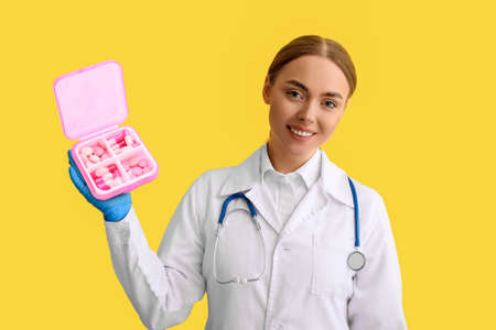 Female doctor holding container with pills on yellow backgroundの写真素材