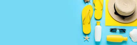 Bottles of sunscreen and beach accessories on light blue background with space for text, top view