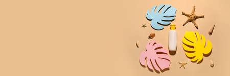 Bottle of sunscreen, decorative tropical leaves and sea shells on beige background with space for...