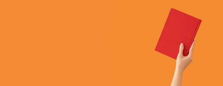 Hand holding book on orange background with space for text