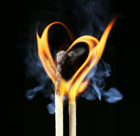 Two burning matches with flame in shape of heart on dark backgroundの写真素材