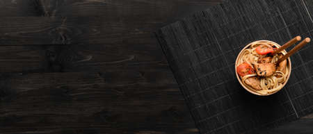 Paper bowl with tasty Chinese noodles and meat on dark wooden background with space for text