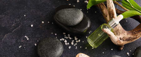 Bottle of essential oil, spa stones and sea salt on dark background, top view