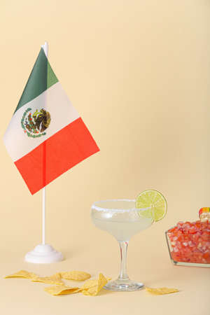 Glass of tasty margarita cocktail with nachos and flag of Mexico on color background