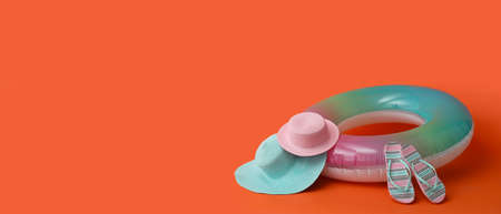 Inflatable ring, beach hats and flip-flops on orange background with space for text