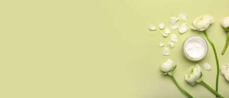 Jar of cosmetic cream and beautiful ranunculus flowers on green background with space for text, top...