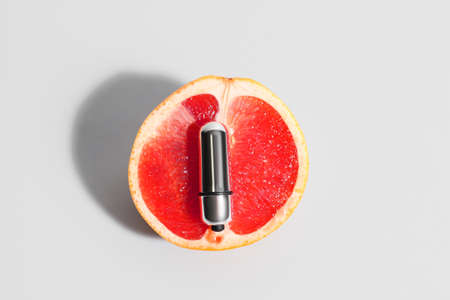 Juicy grapefruit and vibrating bullet from sex shop on light background