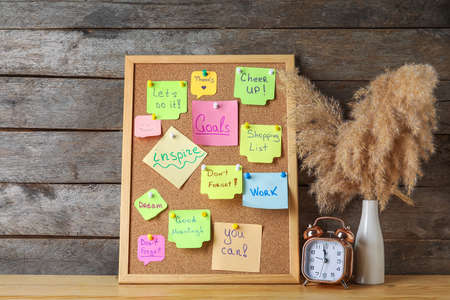 Board with different sticky notes, alarm clock and vase on wooden backgroundの写真素材