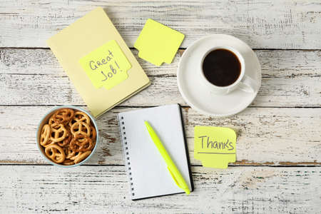 Cup of coffee, snacks and stationery on white wooden background