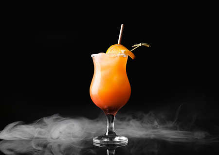 Glass of tasty Tequila Sunrise cocktail and smoke on dark color backgroundの写真素材