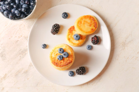 Plate with cottage cheese pancakes and berries on light background