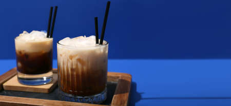 Glasses of White Russian cocktail on blue background with space for text