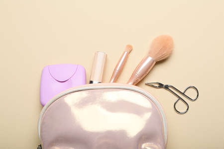 Lady's cosmetic bag with make-up accessories and tampons storage box on beige background