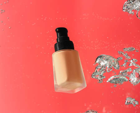 Bottle of makeup foundation in water on color backgroundの写真素材