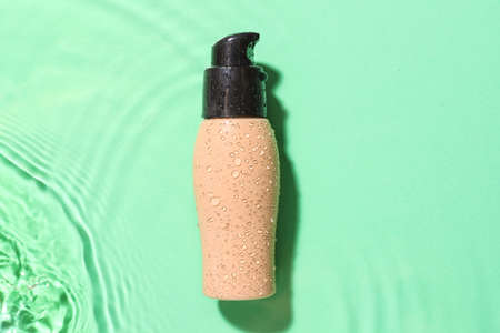 Bottle of makeup foundation in water on color backgroundの写真素材