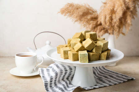 Stand with tasty hojicha marshmallows and cup of tea on light table