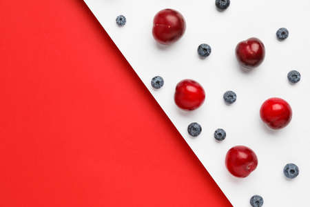 Composition with ripe plums and blueberries on color background