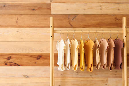 Stand with baby bodysuits near wooden wall