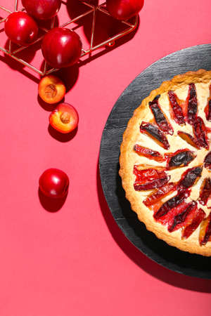 Board with tasty plum pie on color backgroundの写真素材