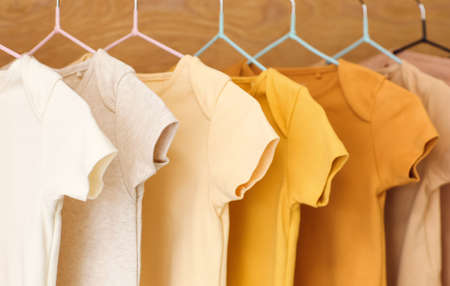 Baby bodysuits hanging near wooden wall, closeup