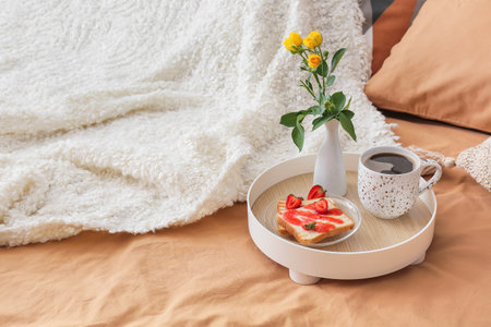 Tray with tasty breakfast and vase with flowers on comfortable bedの写真素材
