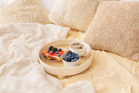 Tray with tasty breakfast on comfortable bed